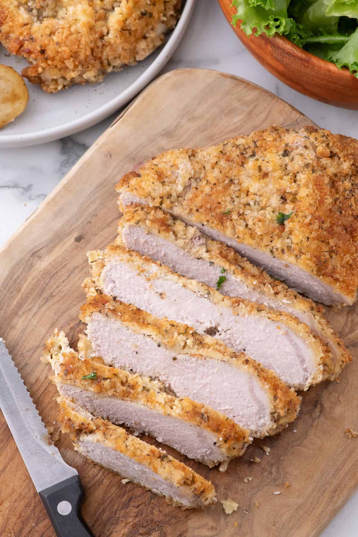 Sliced parmesan crusted pork chop on a wooden cutting board.