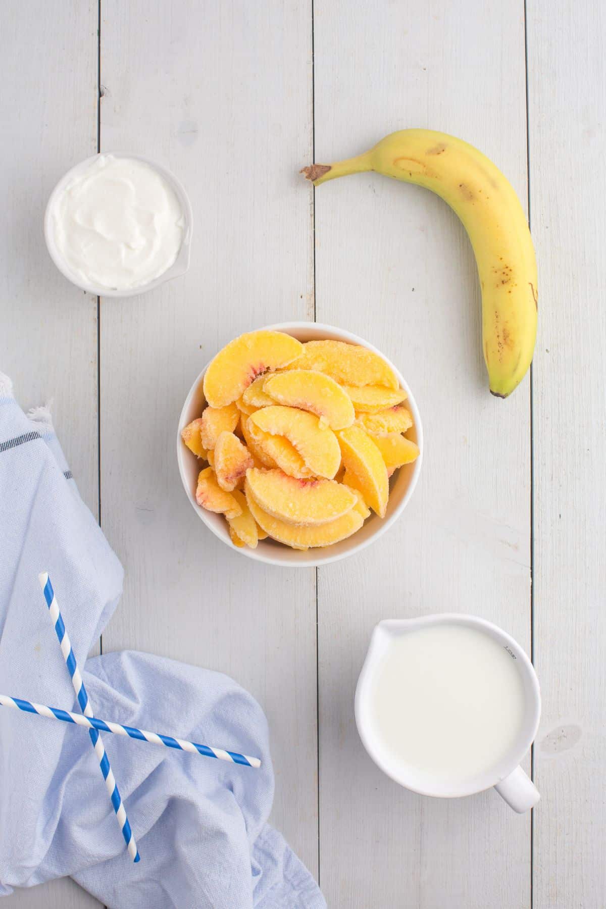 Ingredients for peach smoothie: Vanilla yogurt, milk, a banana, and frozen sliced peaches.