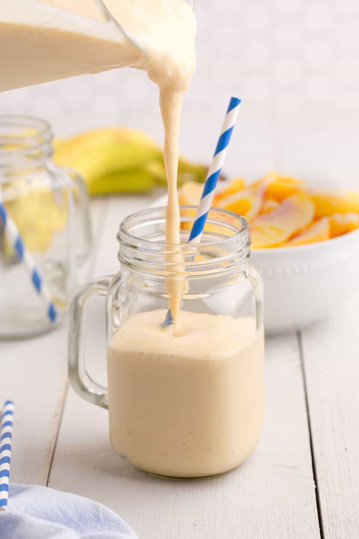 Blender pouring peach smoothie into a glass mug with a blue striped paper straw.