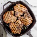 Cast iron pan with cooked and garnished pork chops.