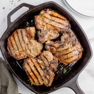 Cast iron pan with cooked and garnished pork chops.