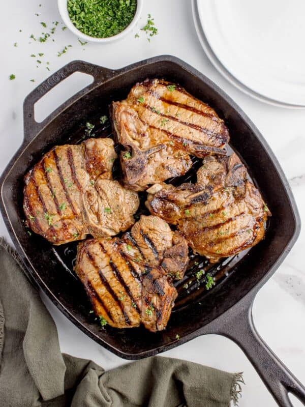 Cast iron pan with cooked and garnished pork chops.