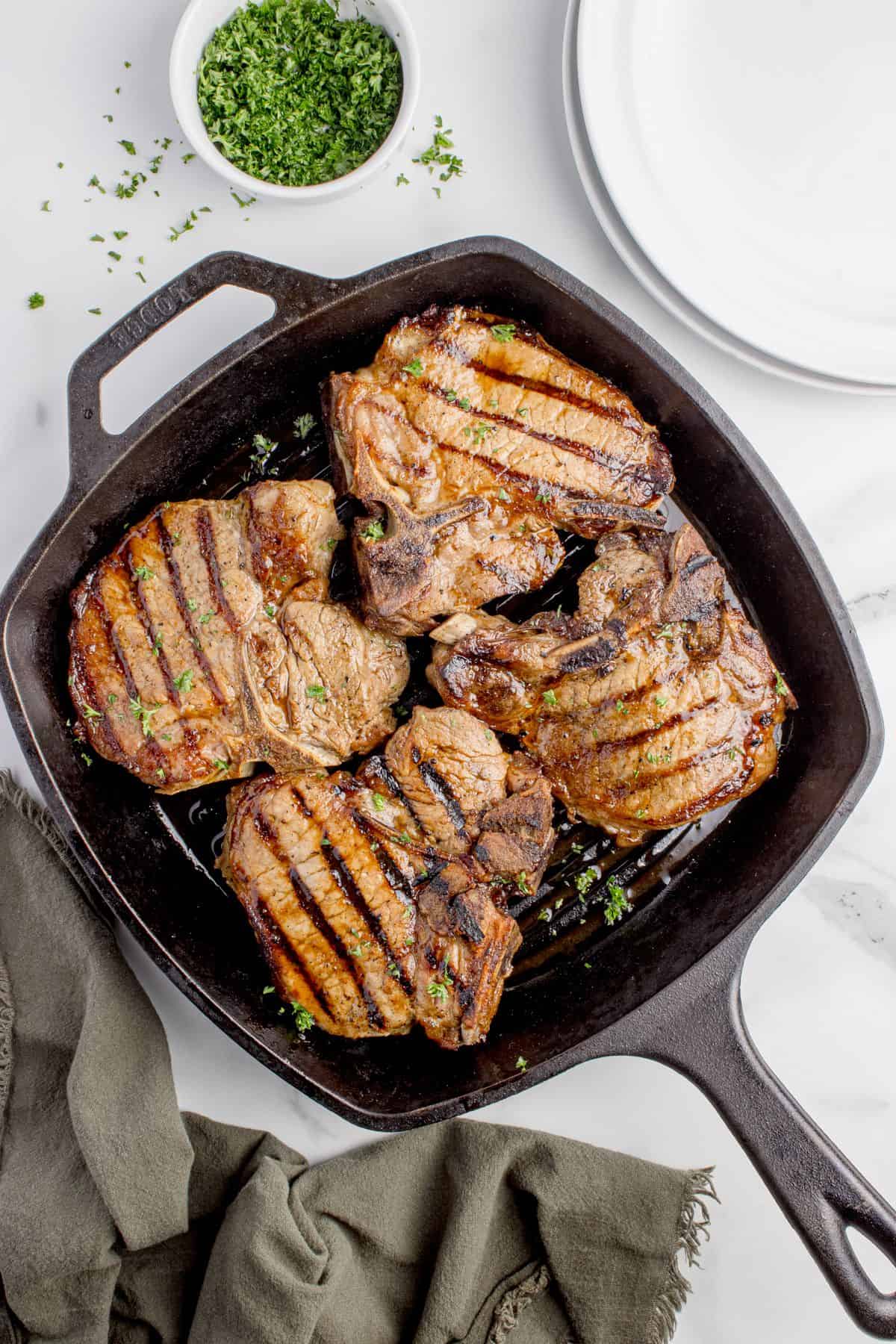 Cast iron pan with cooked and garnished pork chops.