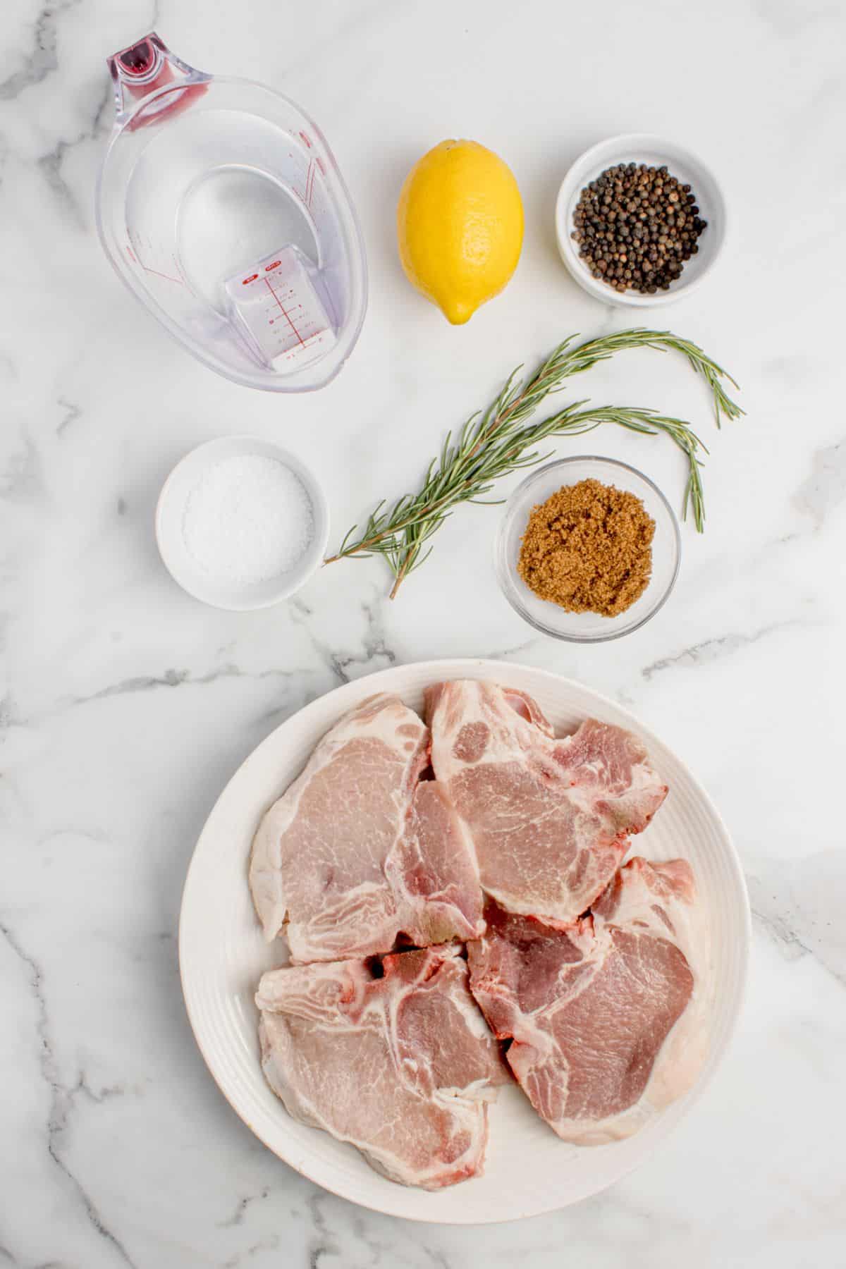 Ingredients for pork chop brine: water, salt, brown sugar, peppercorns, lemon juice, rosemary sprigs, bay leaves, and bone-in pork chops.