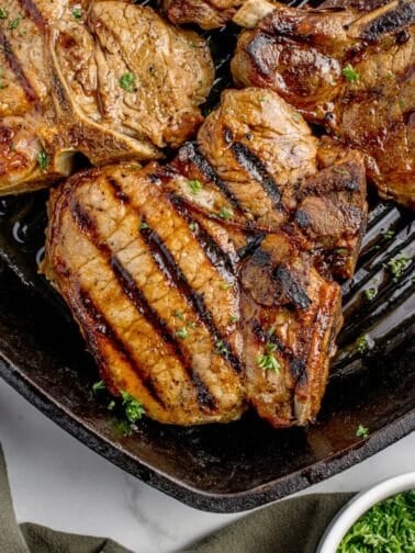 Completed pork chops in a cast iron pan garnished with parsley.