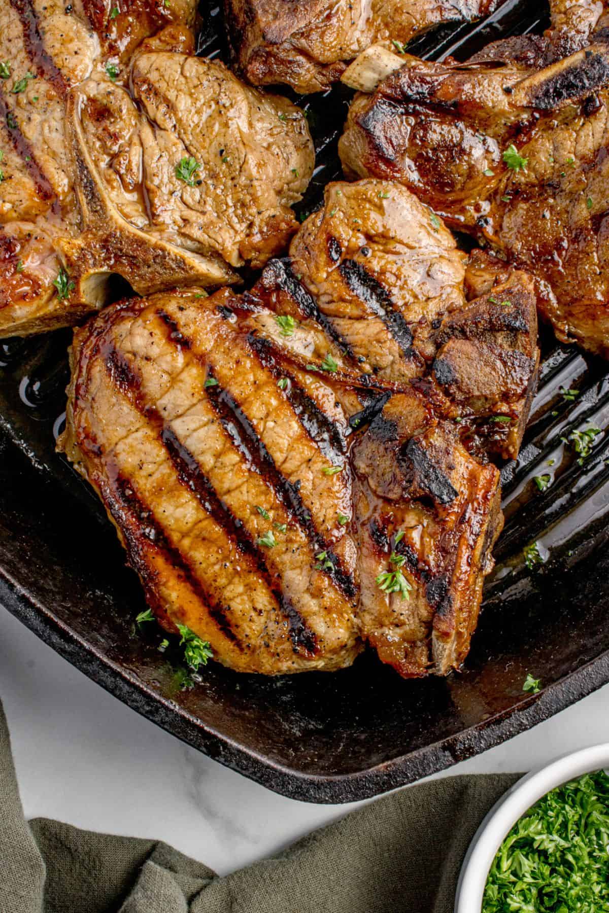 Completed pork chops in a cast iron pan garnished with parsley.