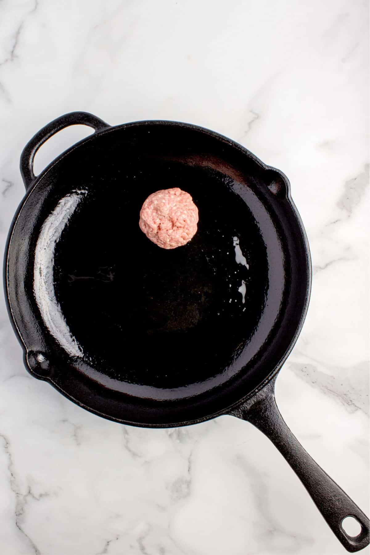 A loose ball of raw ground beef is placed in a cast iron pan for smashing.