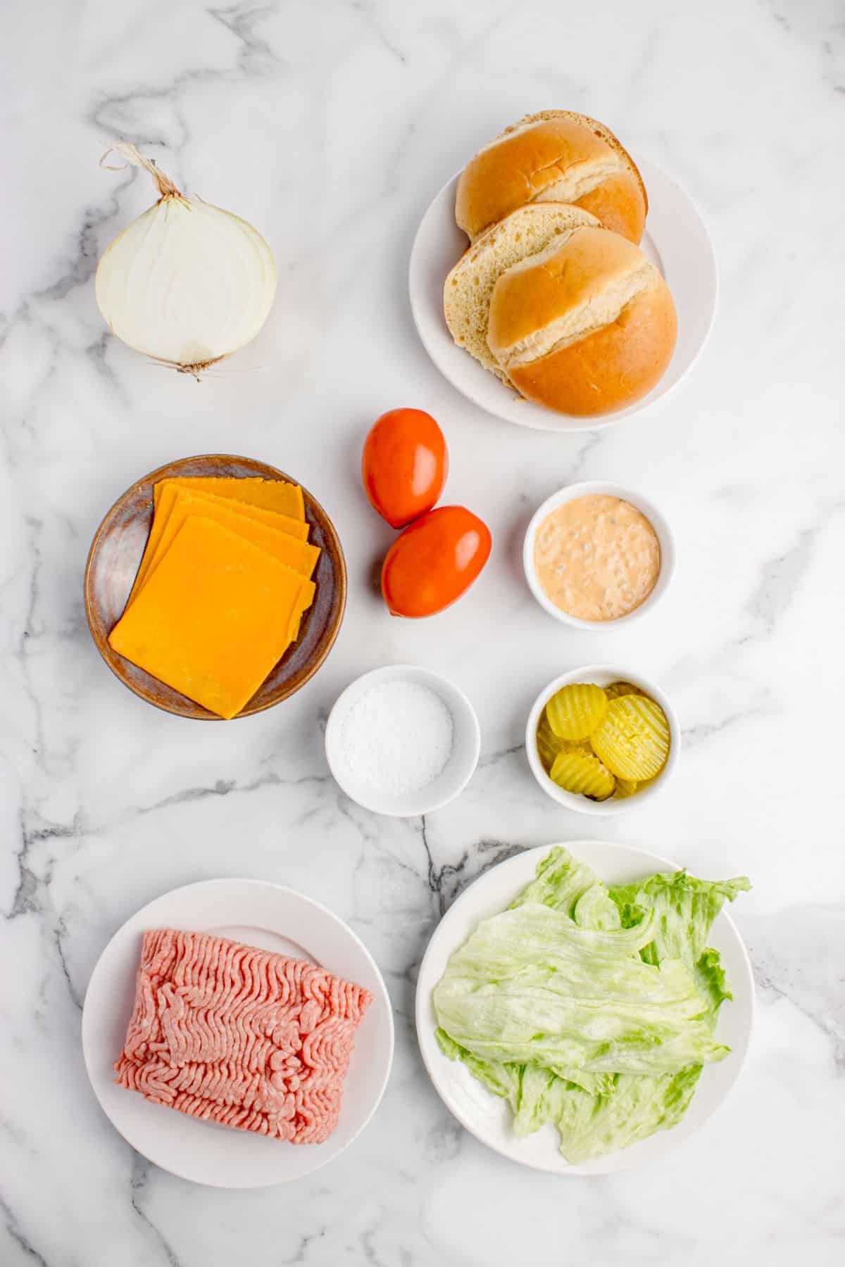 Ingredients for smash burgers: hamburger buns, onion, tomato, cheese, smash burger sauce, pickles, salt, ground beef, and lettuce.
