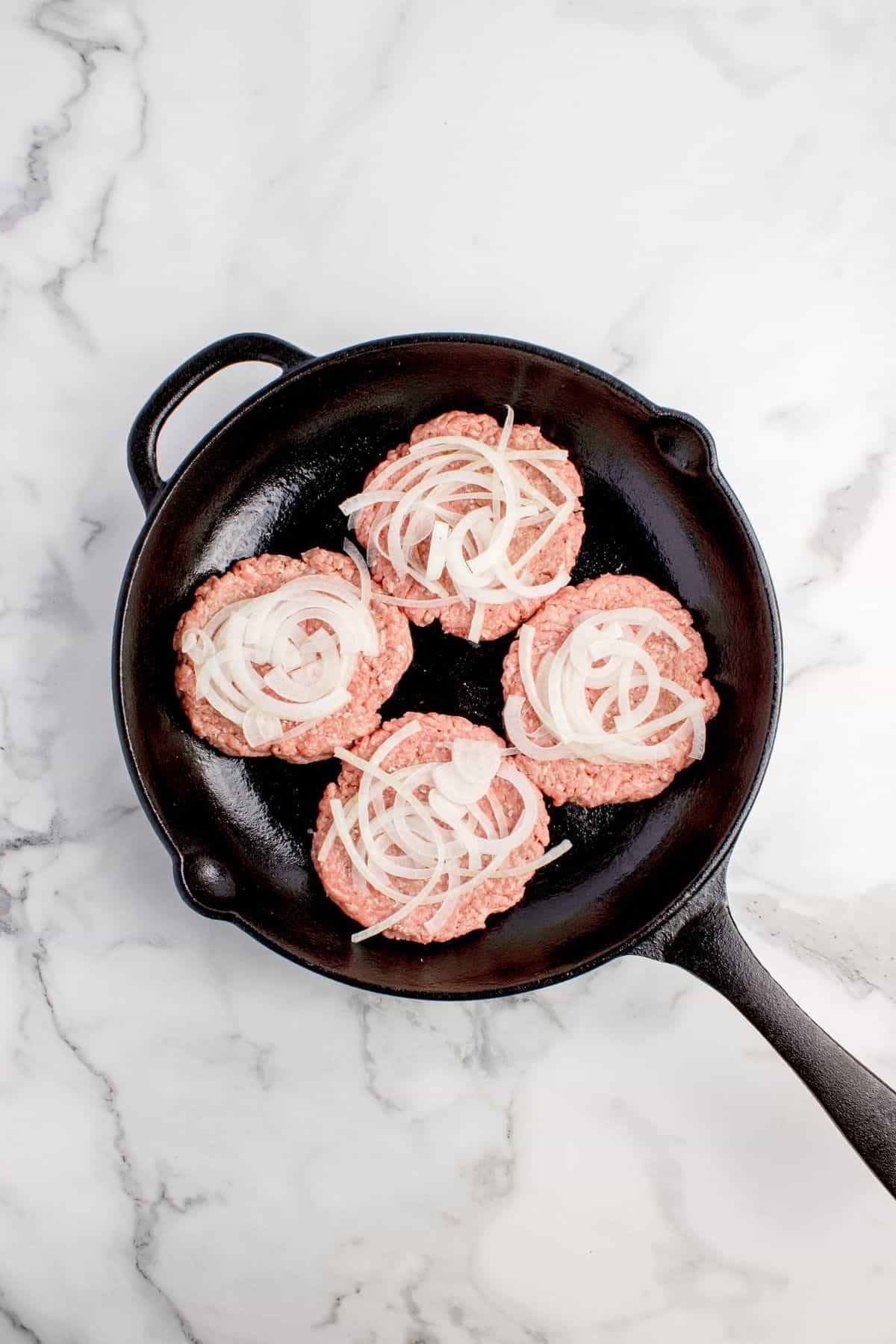 Raw onions layered on raw ground beef patties.