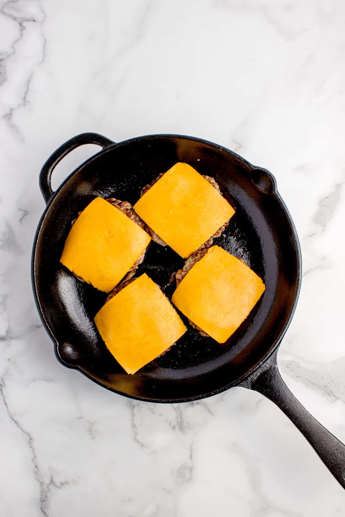 Cheese slices added to the cooked burgers.