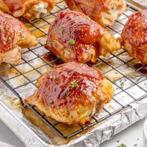 Closeup of the baked BBQ chicken thighs on a wire rack over a baking sheet.