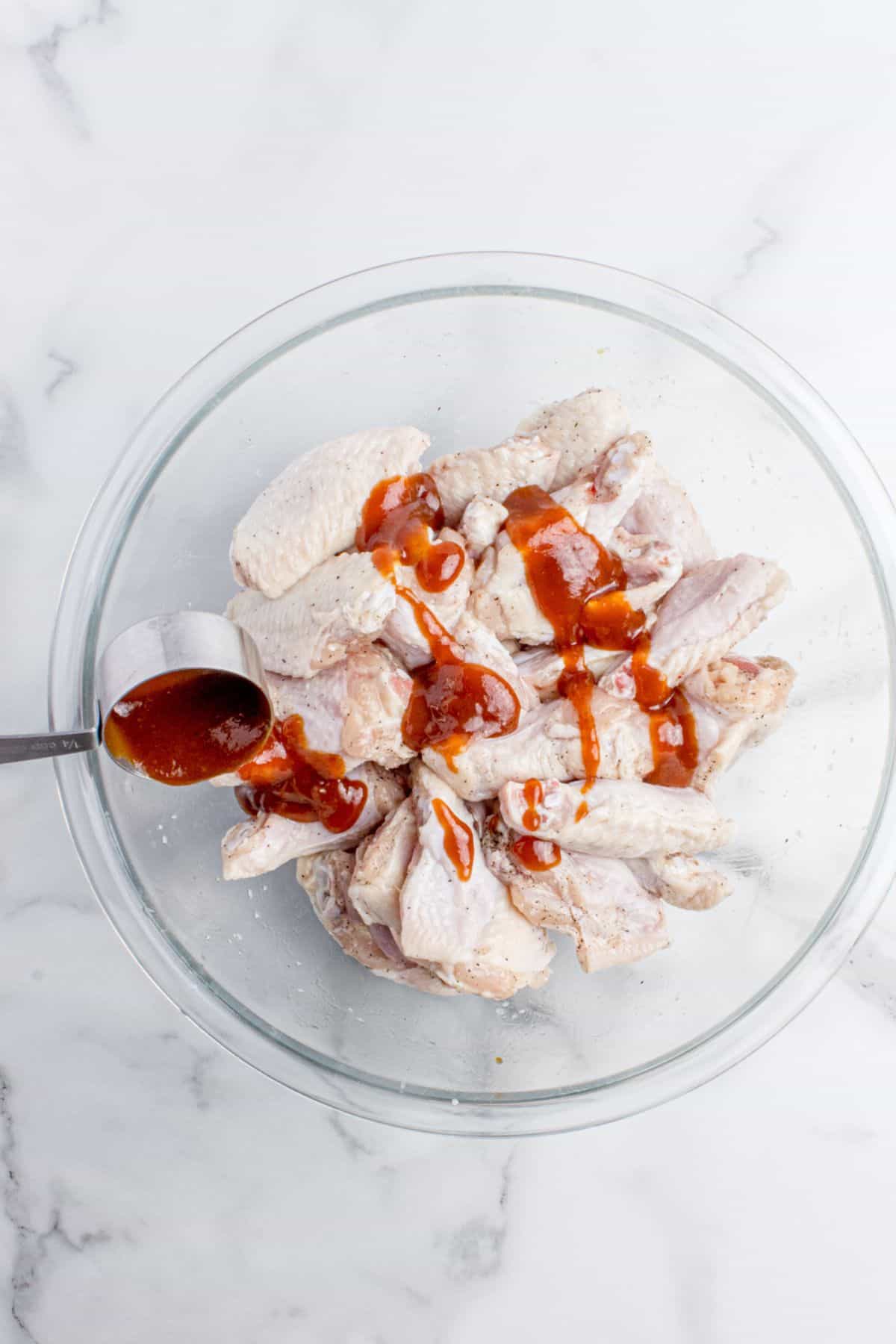 Chicken wings with BBQ sauce being put on them in a bowl.