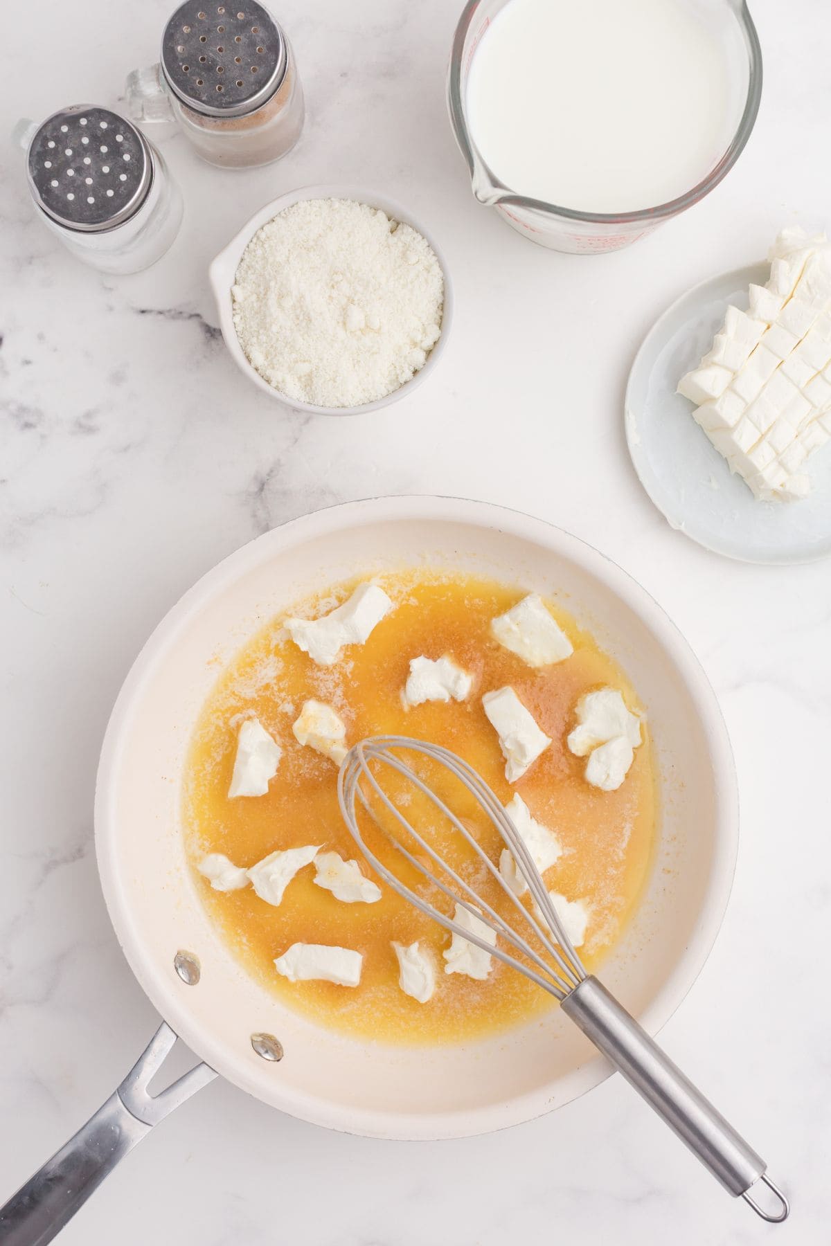 Chunks of cream cheese melting in a skillet with butter and garlic powder.