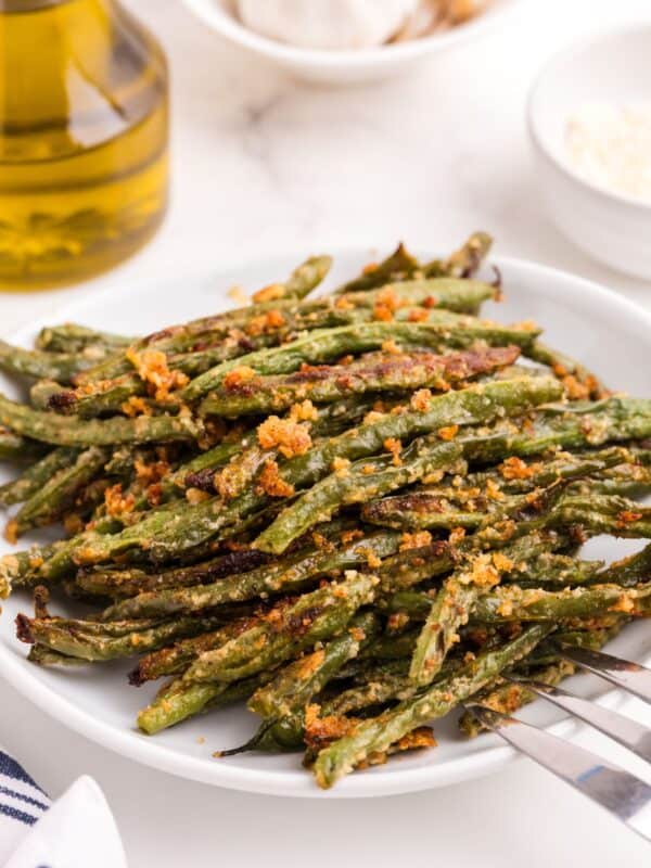 Baked green beans on a serving plate with a large serving fork.
