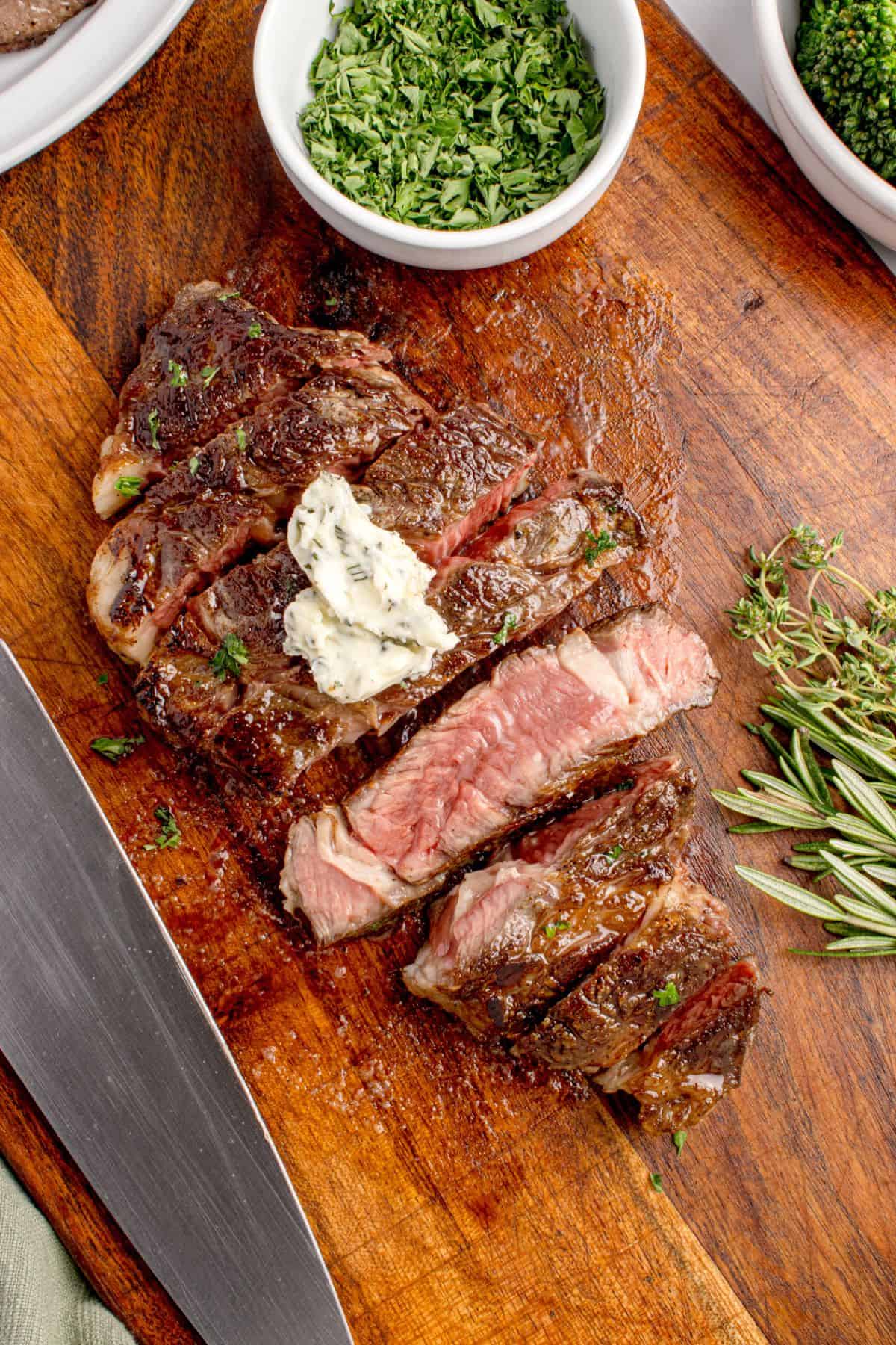 Sliced beef chuck eye steak on a wooden cutting board. One slice is turned sideways to show the interior of the steak.