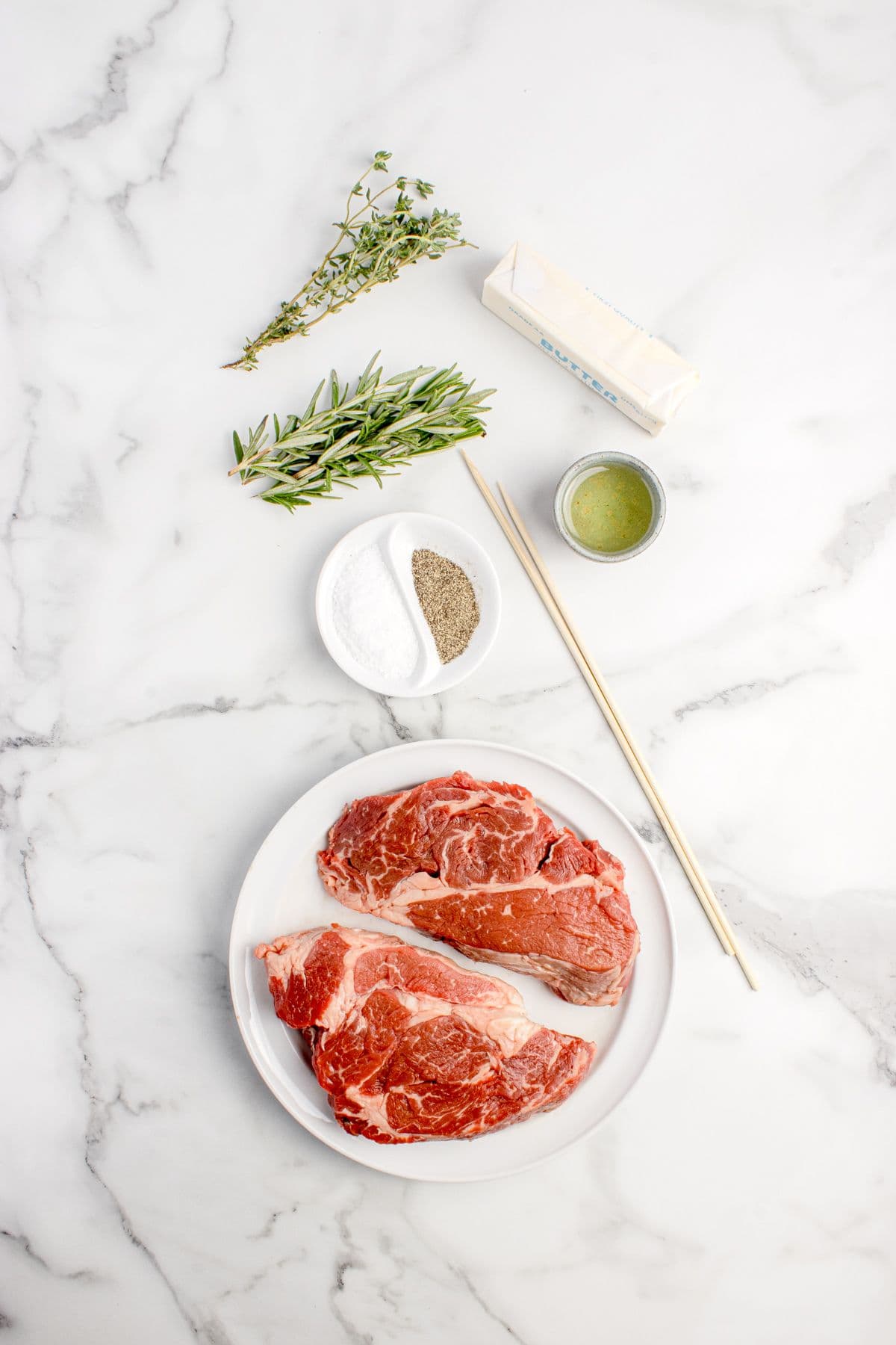 Ingredients for beef chuck eye steak: Steaks, salt, pepper, olive oil, butter, fresh rosemary, and fresh thyme.
