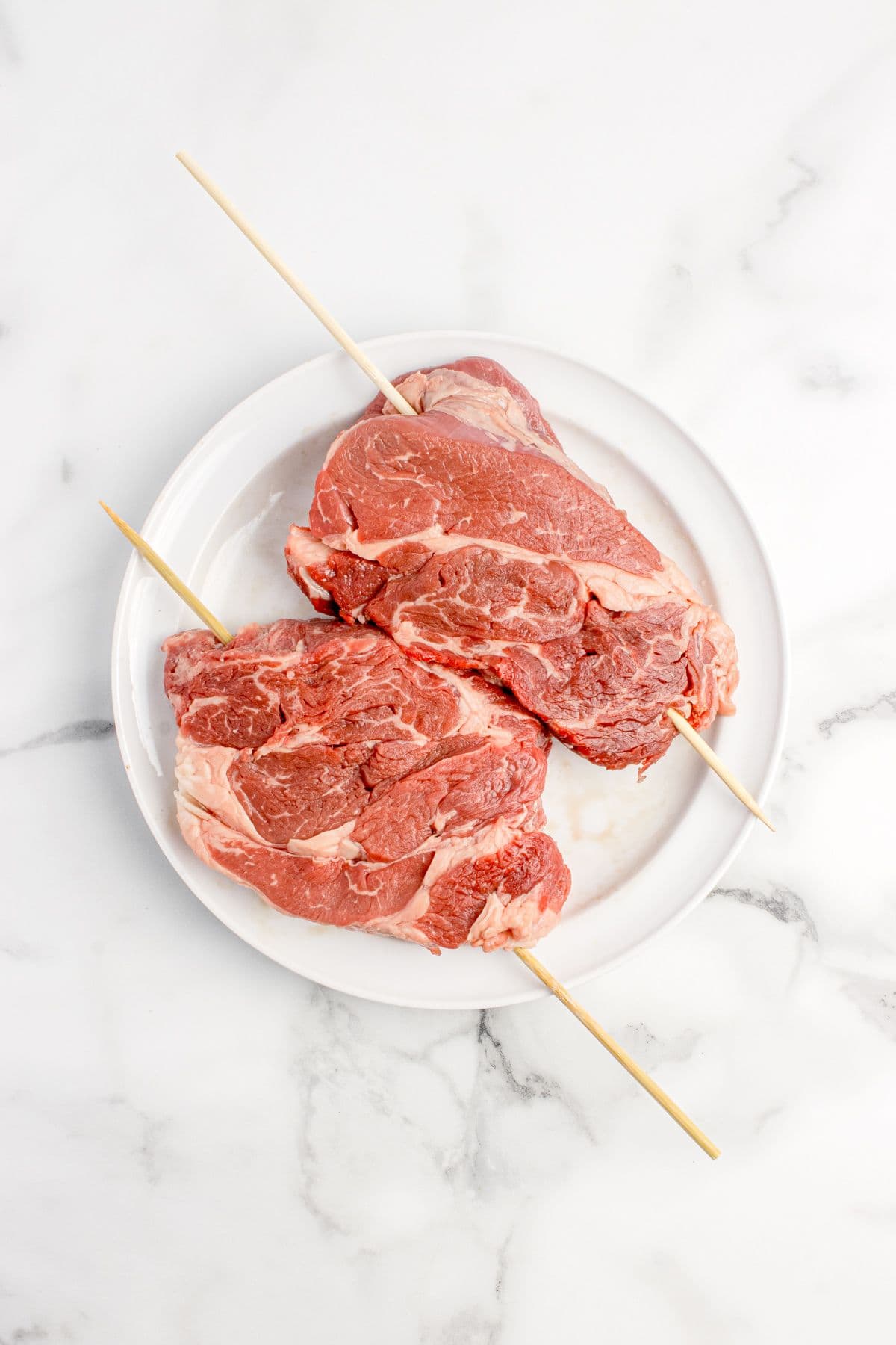 Beef chuck eye steaks with skewers stuck through them lengthwise.