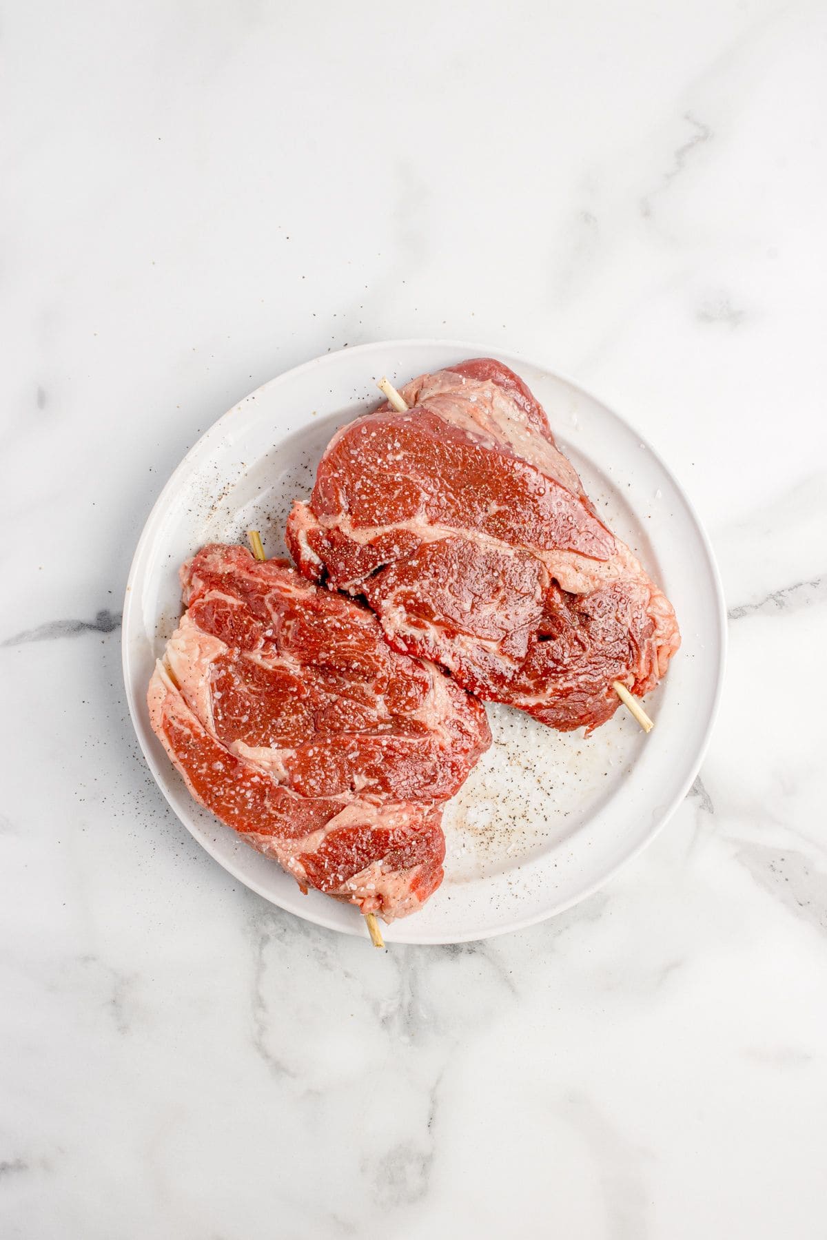 Skewered and seasoned steaks on a white plate.