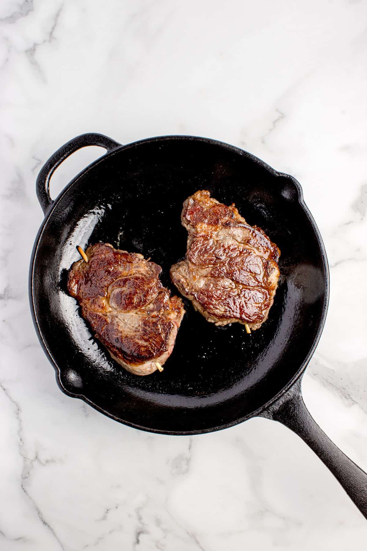 Cooked and skewered steaks in a cast iron pan.