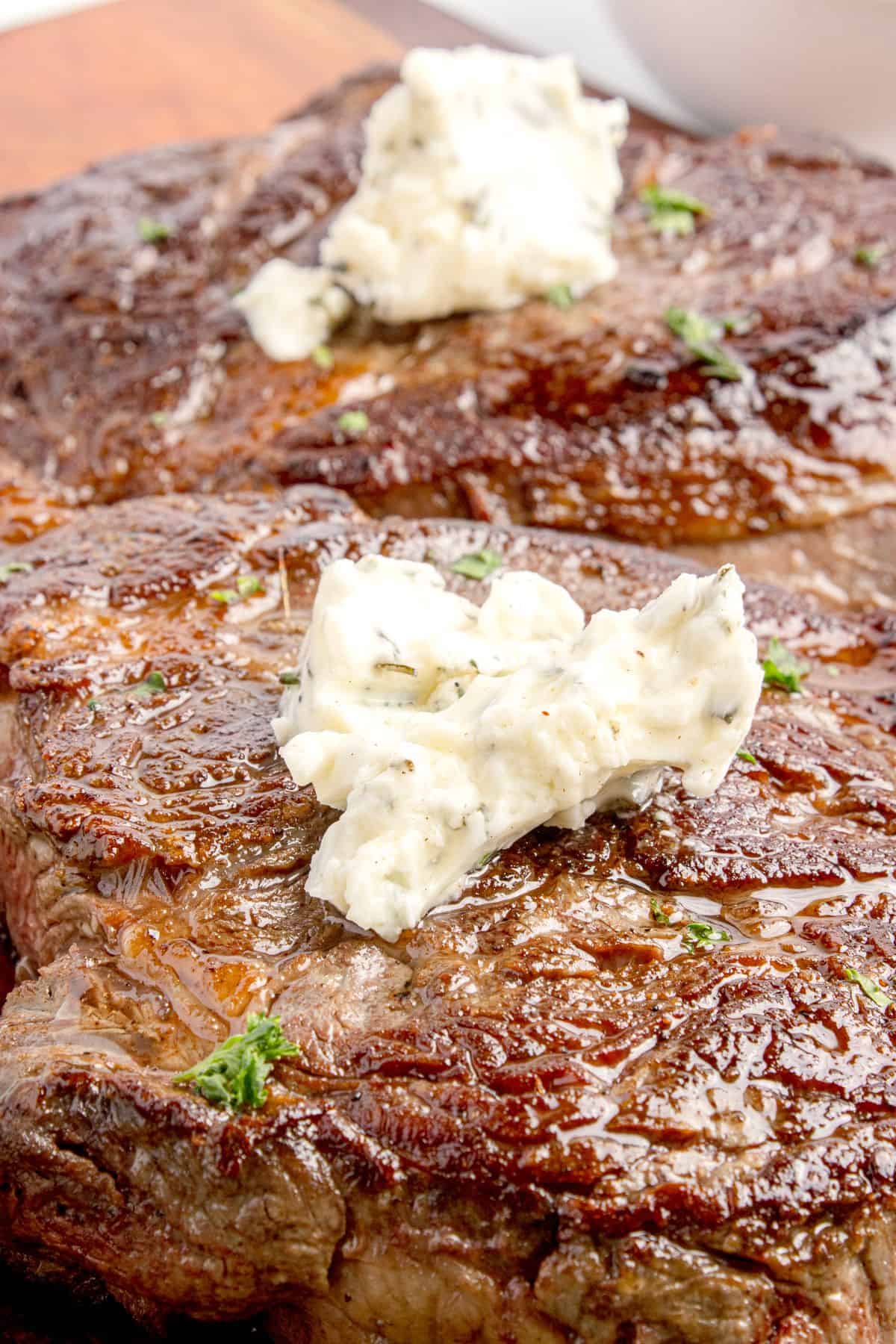 Cooked chuck eye steaks with a pat of butter on top of each.