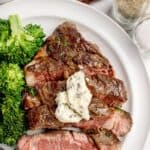 Cooked and sliced beef chuck eye steak on a white dinner plate with a side of broccoli.