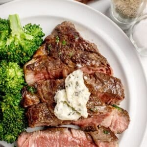 Cooked and sliced beef chuck eye steak on a white dinner plate with a side of broccoli.