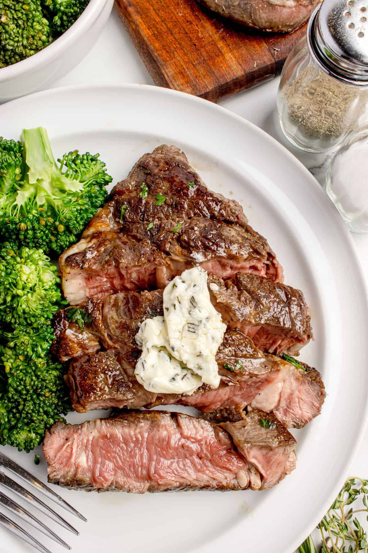 Cooked and sliced beef chuck eye steak on a white dinner plate with a side of broccoli.