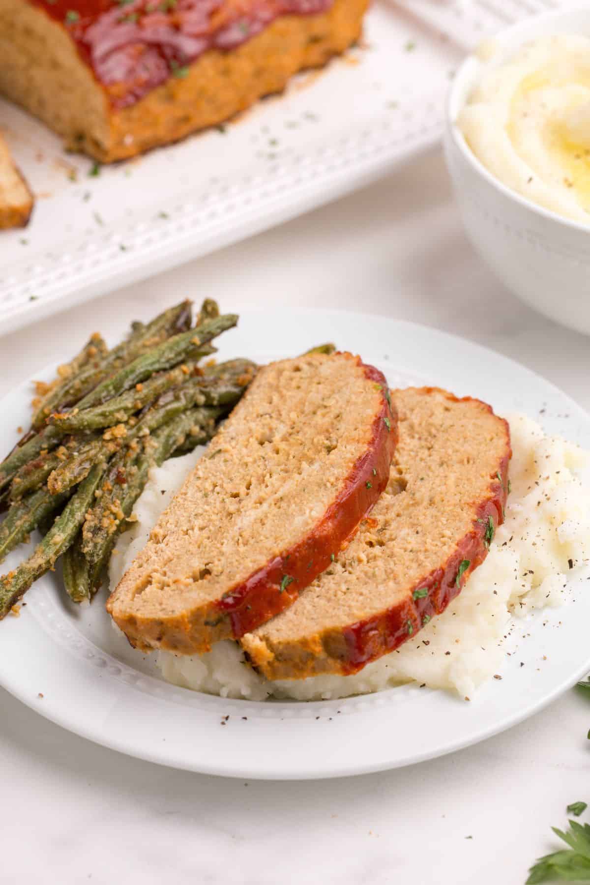 Two slices of chicken meatloaf on a white dinner plate with mashed potatoes and asparagus.