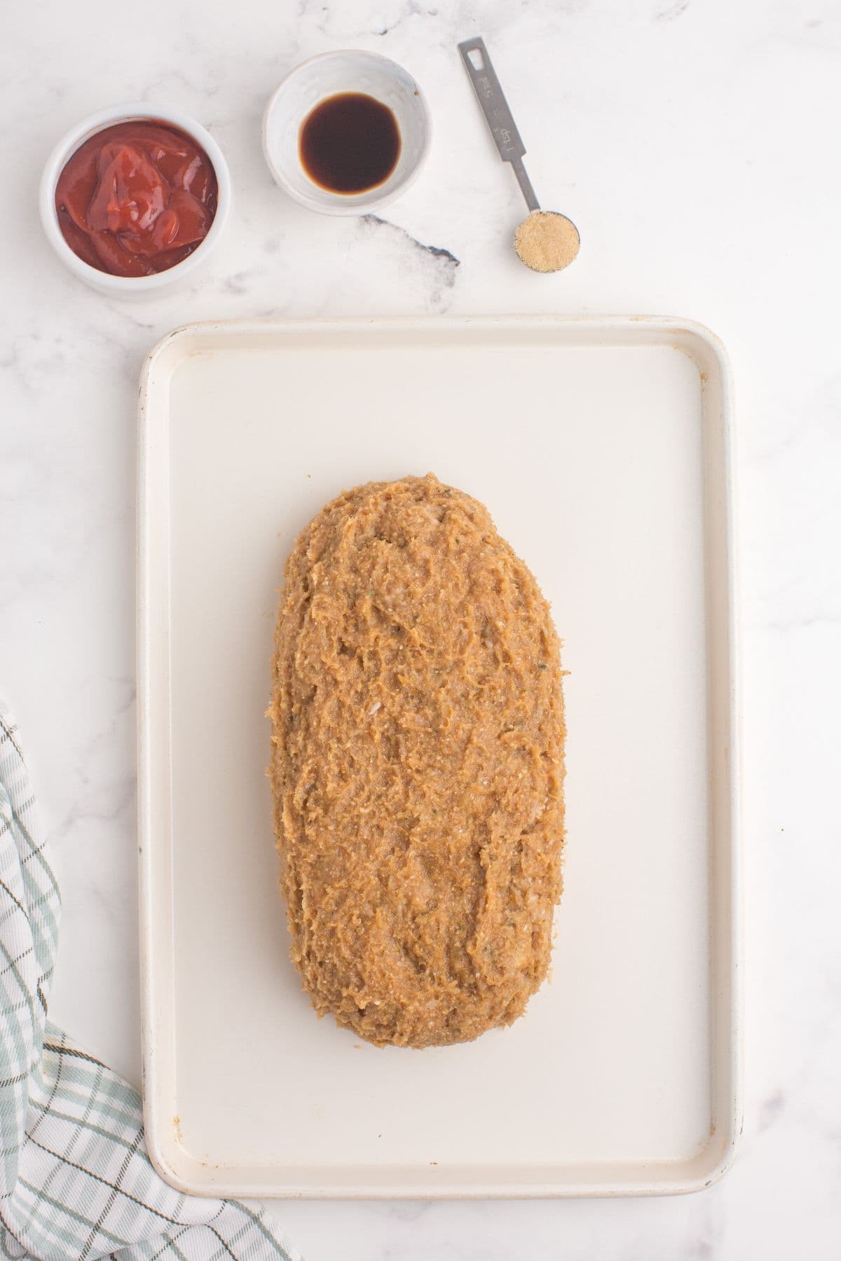 Chicken is formed into the shape of a meatloaf on a white baking sheet.