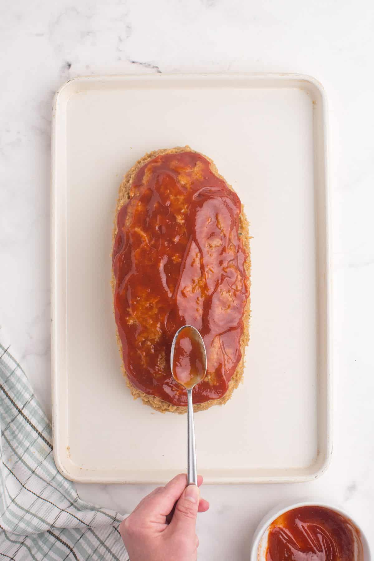 Sauce is spooned and spread on top of the raw chicken meatloaf.