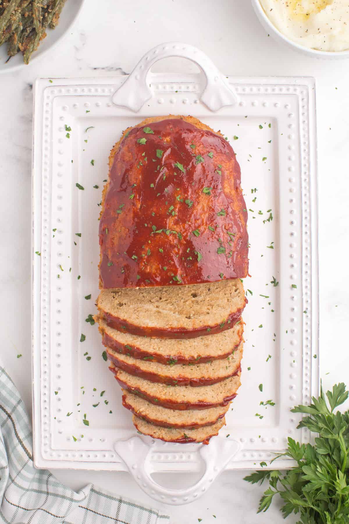 Chicken meatloaf on a white serving platter with a parsley garnish.