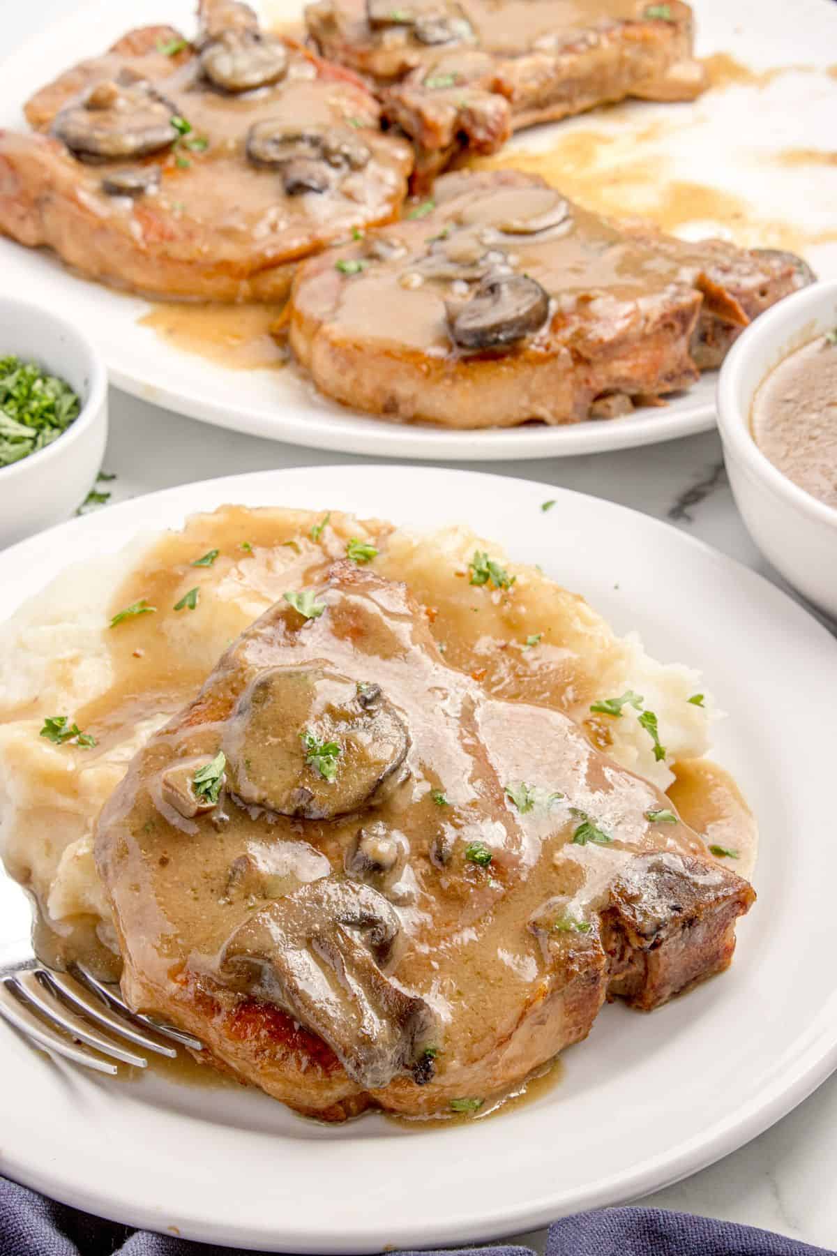 Crock pot pork chops with mushroom gravy on a white dinner plate with a side of mashed potatoes.