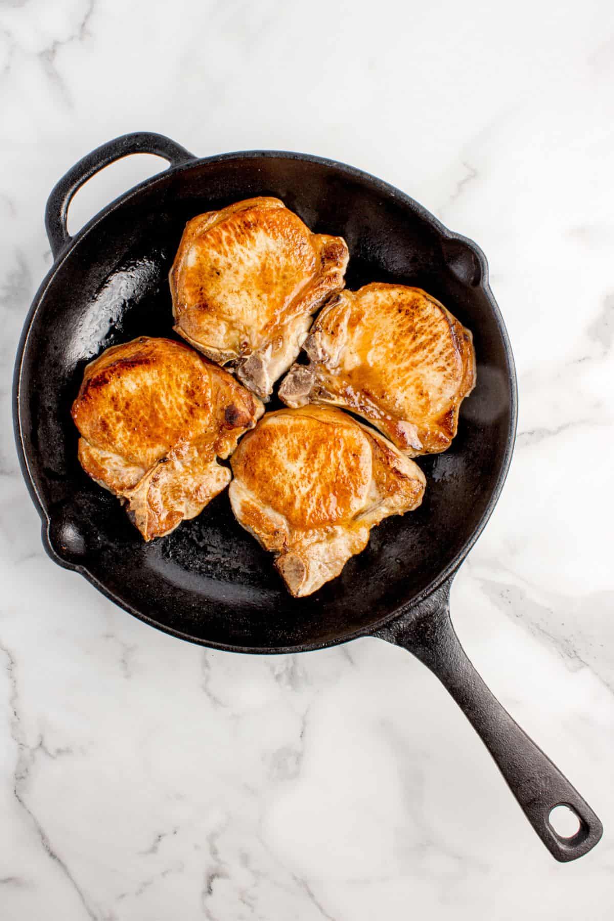 A cast iron pan with seared pork chops in it.