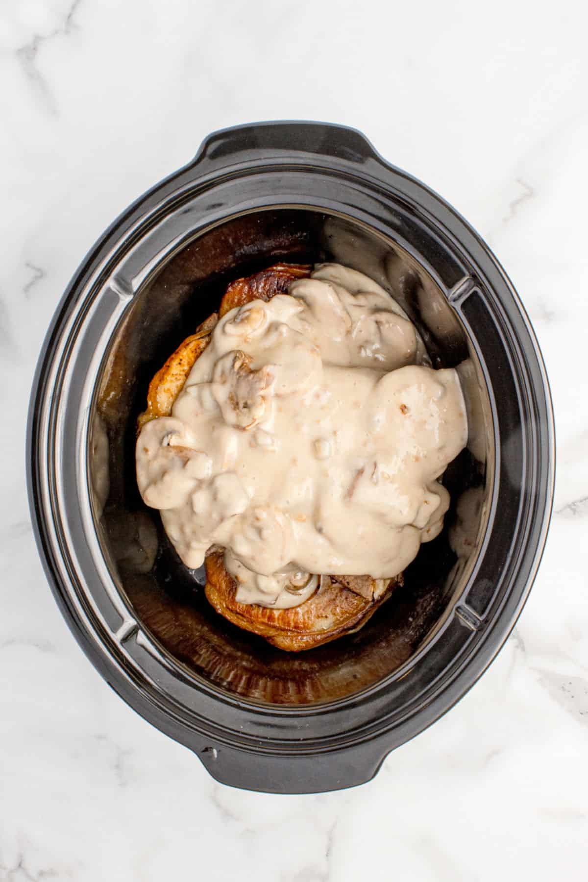 Crock pot liner with seared pork chops at the bottom and the mushroom gravy on the top.