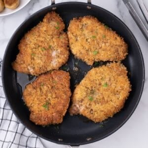 Parm crusted pork chops in an oven safe pan cooked and golden brown.