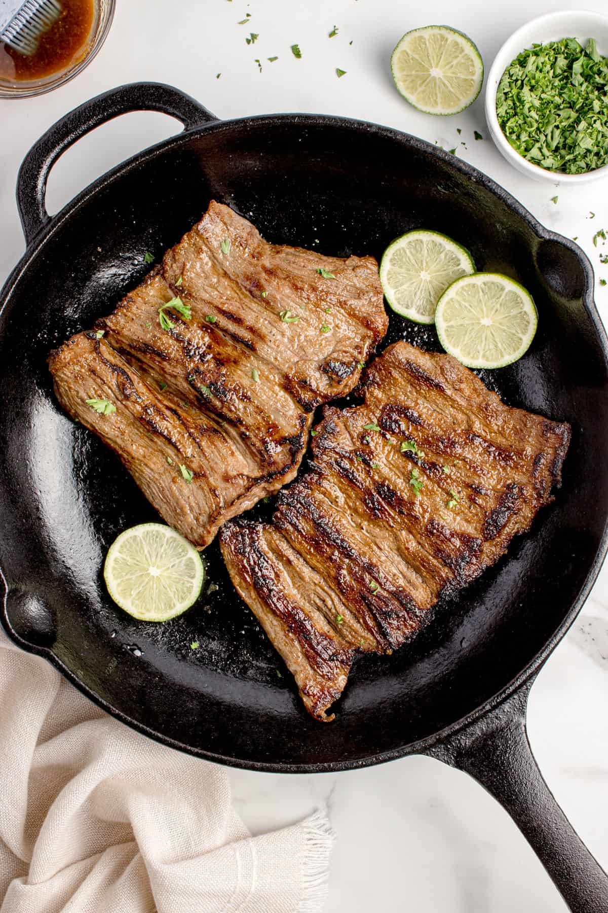 Skirt steak in a cast iron pan garnished with sliced limes.