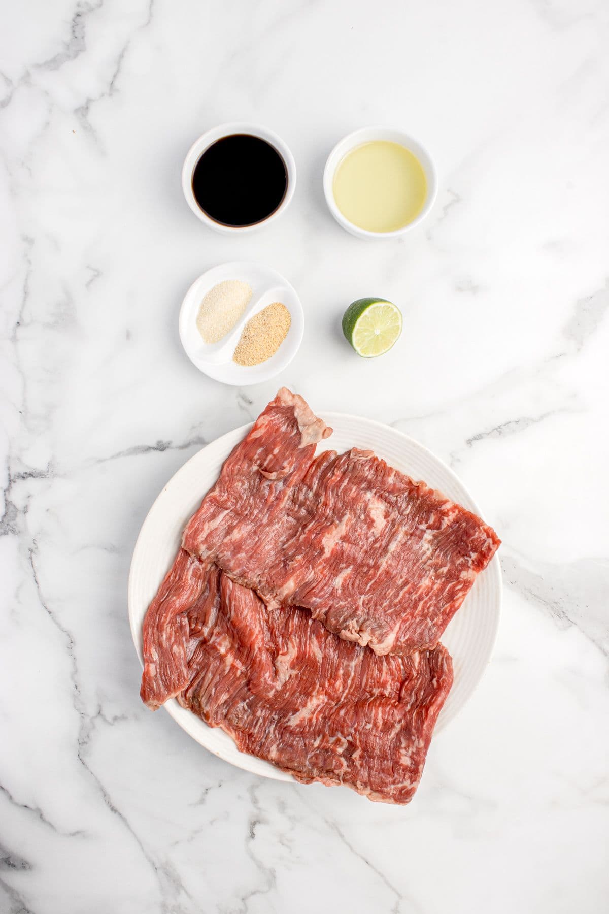 Ingredients for skirt steak marinade: Skirt steak, lime, garlic powder, onion powder, soy sauce, and olive oil.