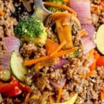 Stir fry on a serving spoon lifted above the cast iron pan.