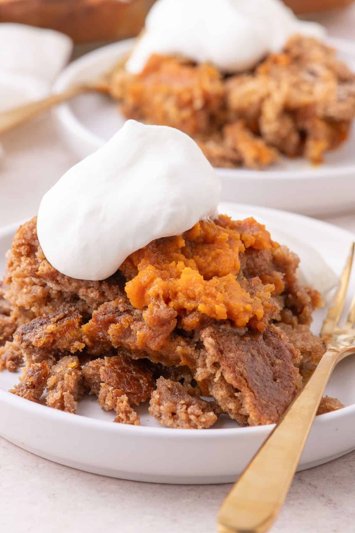 A serving of pumpkin dump cake on a white plate with a dollop of whipped cream.
