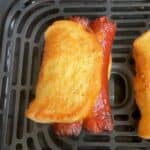Closeup of the air fryer grilled cheese hot dogs to show the golden brown on the outside, in an air fryer basket.