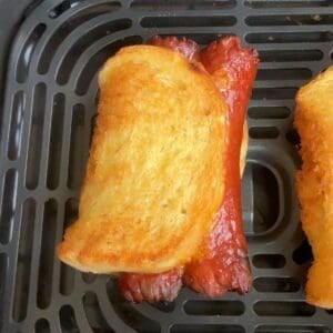 Closeup of the air fryer grilled cheese hot dogs to show the golden brown on the outside, in an air fryer basket.