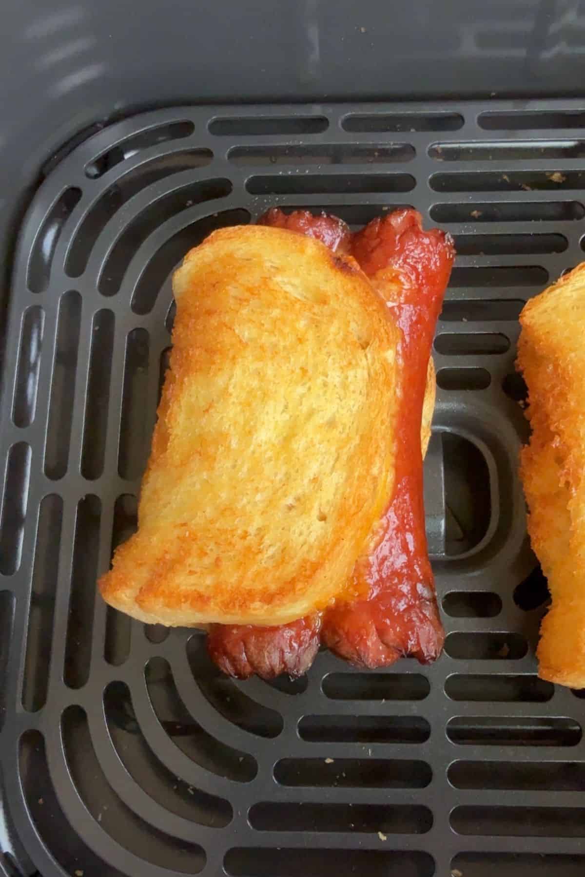 Closeup of the air fryer grilled cheese hot dogs to show the golden brown on the outside, in an air fryer basket.