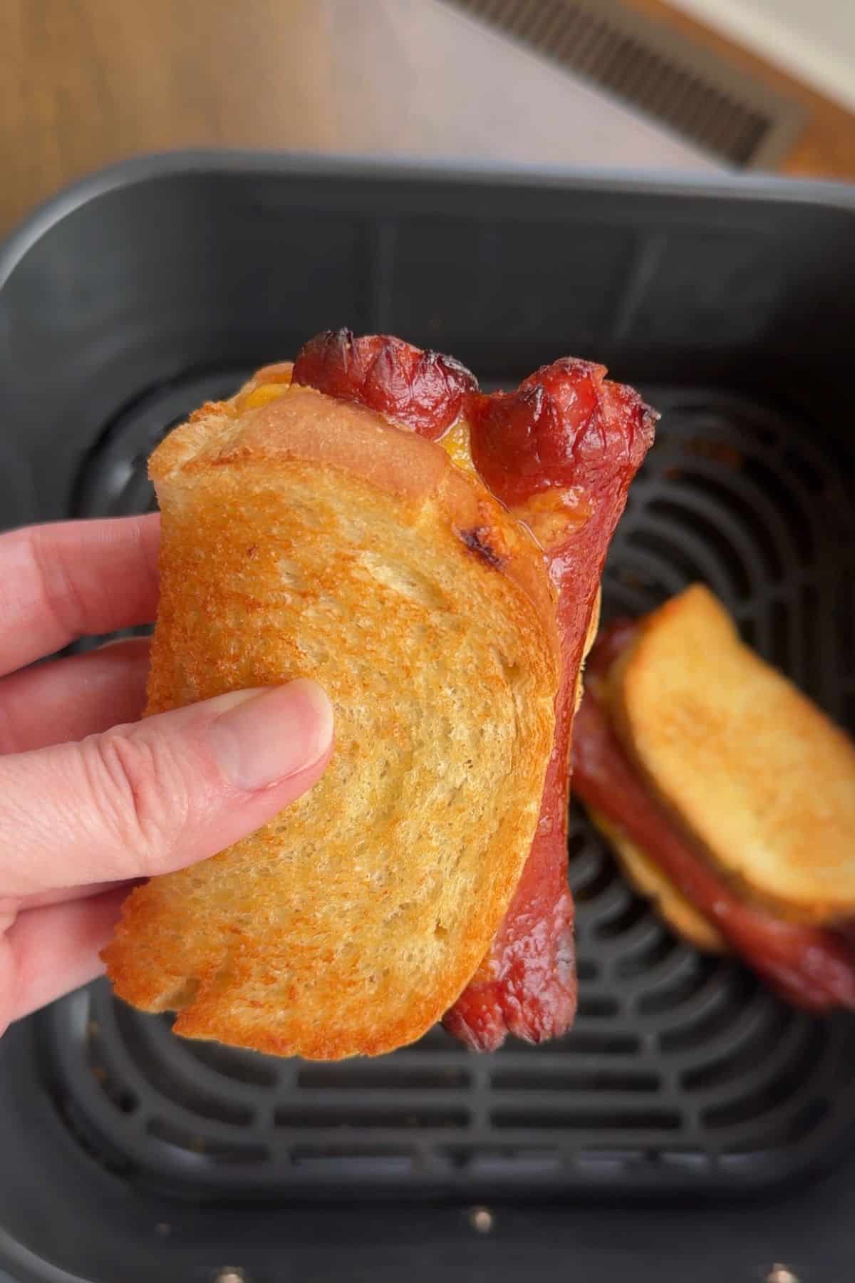 Air fryer grilled cheese hot dog being held up to show the cheesiness, golden brown outside, and cooked hot dog.