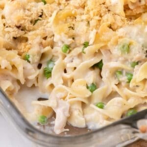 Tuna casserole in a glass baking dish. A serving has been removed from the corner of the baking pan.